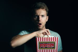 Portrait Of Surprised Man Eating Popcorn Against Black Background