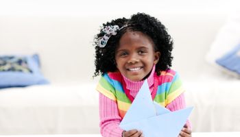 Smiling little girl at home with a paper boat