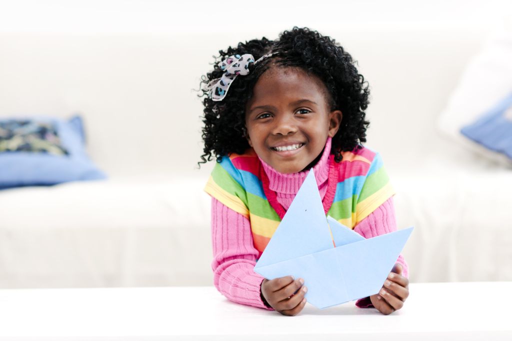 Smiling little girl at home with a paper boat