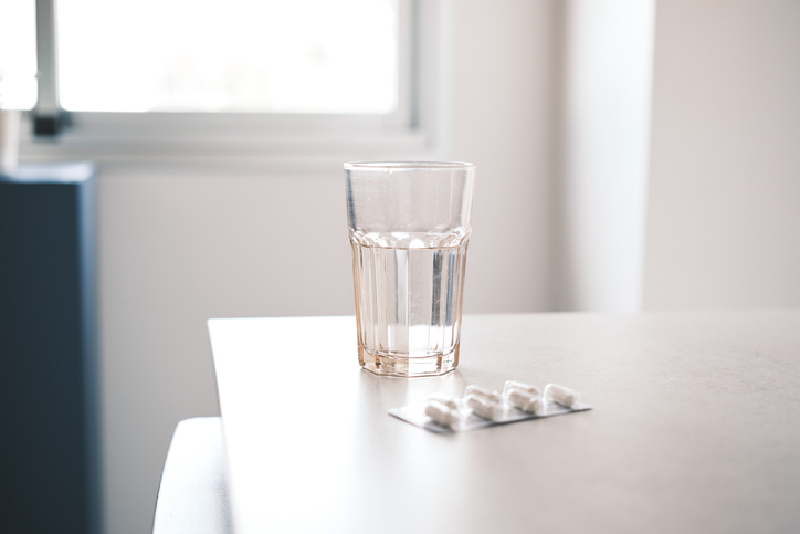 Glass of water and pills on kitchen counter. Medications