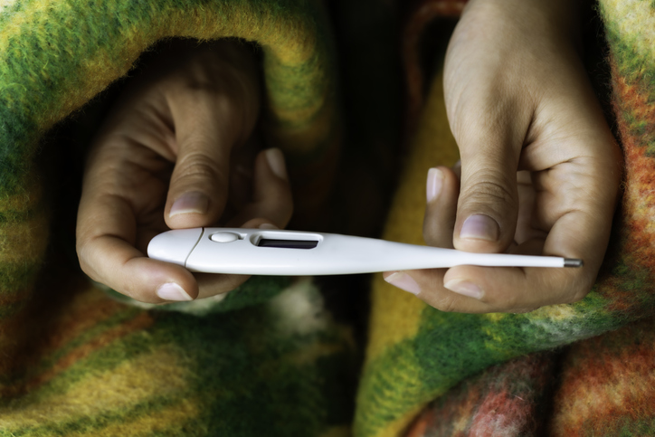 Hands Holding a Digital Thermometer Under a Blanket