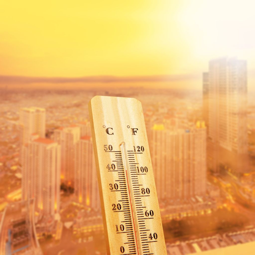 Thermometer shows a high temperature reading against the blurred background of a city skyline during a sunny, hot day. Heatwave and global warming in an urban environment. Extreme weather background