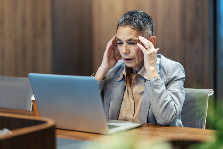 Mature adult woman experiencing stress and headache using laptop