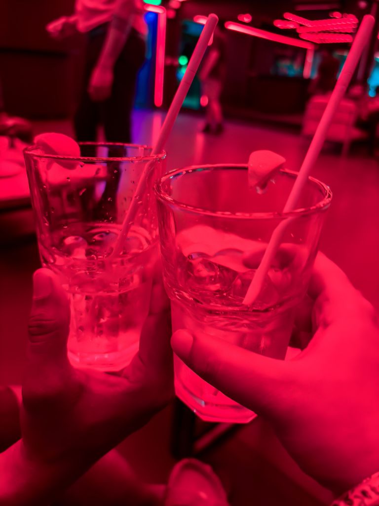 friends toasting cocktails in neon nightclub party atmosphere with red lighting