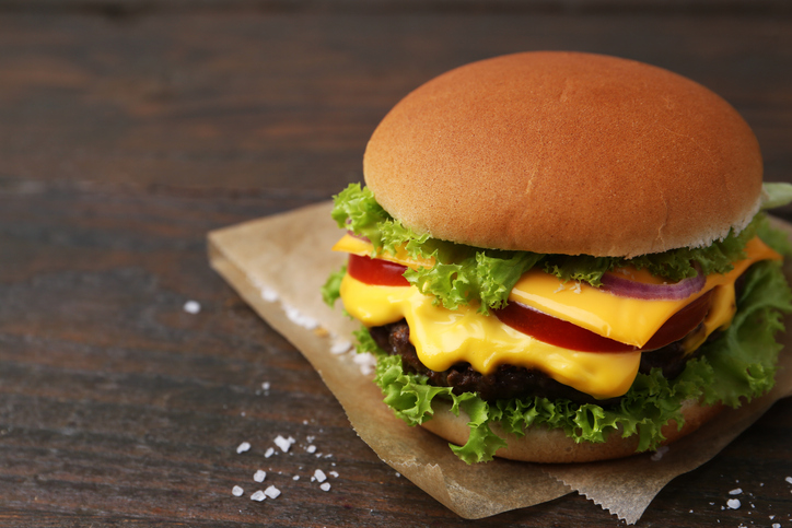 Tasty cheeseburger on wooden table, closeup. Space for text