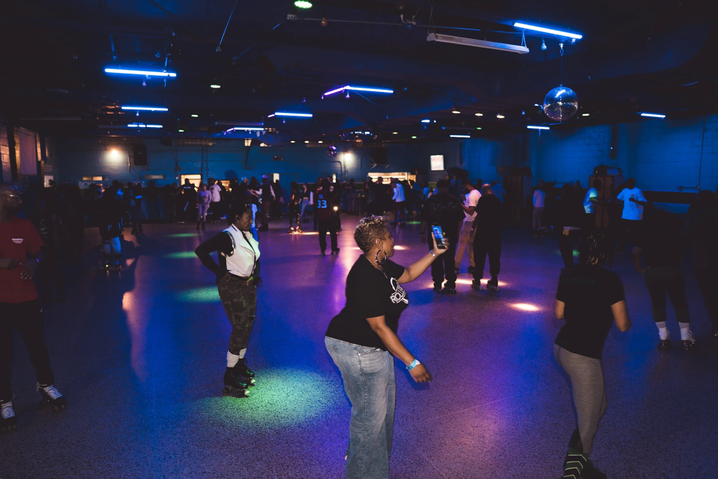 A crowded dance floor with people dancing under colorful neon lights and a disco ball.